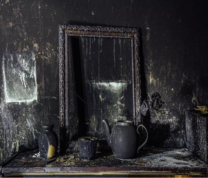 Burnt room with charred wall, picture frame, pot with burned rose in black soot   