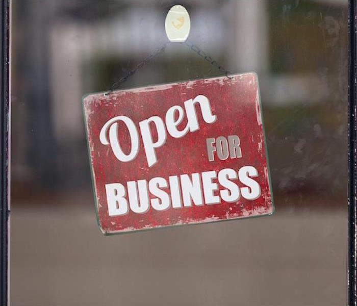 Red sign hanging on a window that says Open for business 