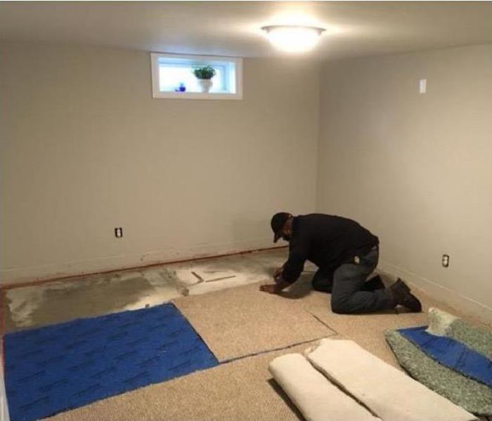Man removing water damaged carpeting and padding in room