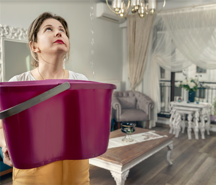a woman holding a bucket to catch water falling from her ceiling